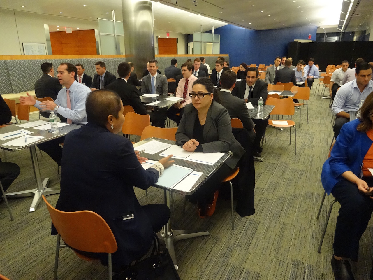 people sitting in a large room, at tables for two, talking