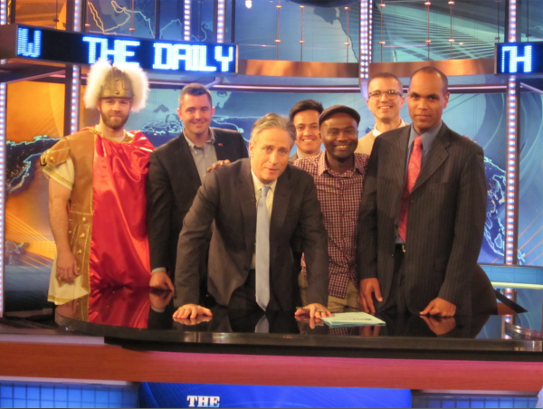 Jon Stewart with 6 of the veterans posing behind the Daily Show desk